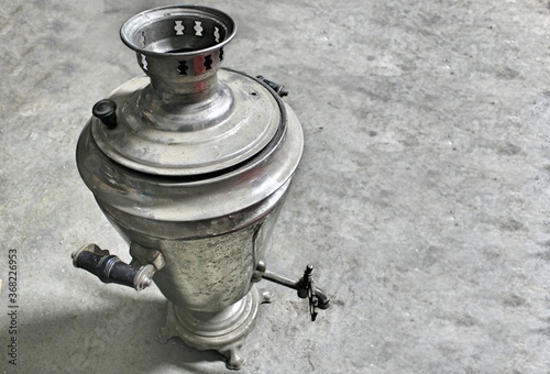 One old worn steel samovar on a gray concrete floor.