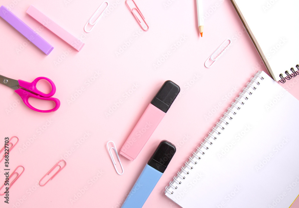 White notepad, pink and blue markers, paper clips, scissors, eraser on pink background with space for text. School stationery and supplies. Back to school, homeschool creative workspace. Flat lay