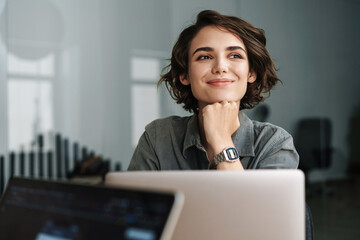 Image of young beautiful joyful woman smiling while working with laptop