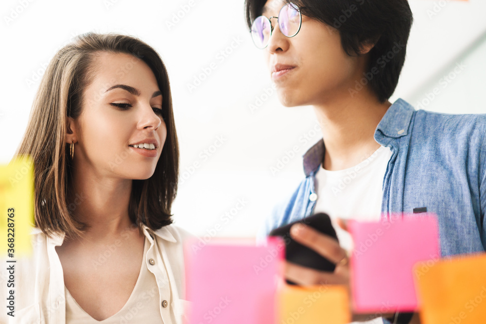 Image of multinational pleased colleagues using mobile phone and talking Image of multinational pleased colleagues using mobile phone and talking