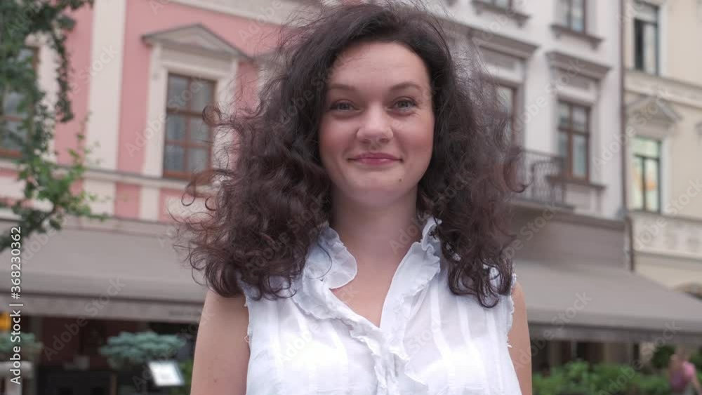 Portrait young attractive smile woman with curly hair look at camera at city center feel happy. Joy of life, active lifestyle. Slow motion 4k Portrait young attractive smile woman with curly hair look at camera at city center feel happy. Joy of life, active lifestyle. Slow motion 4k