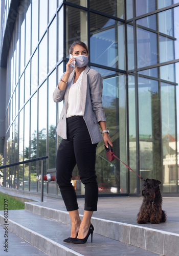Business woman walking dog on leash and talking on phone