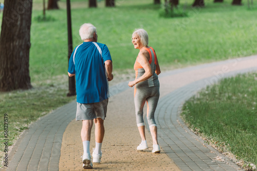 Back view of smiling senior woman looking at husband while jogging in park