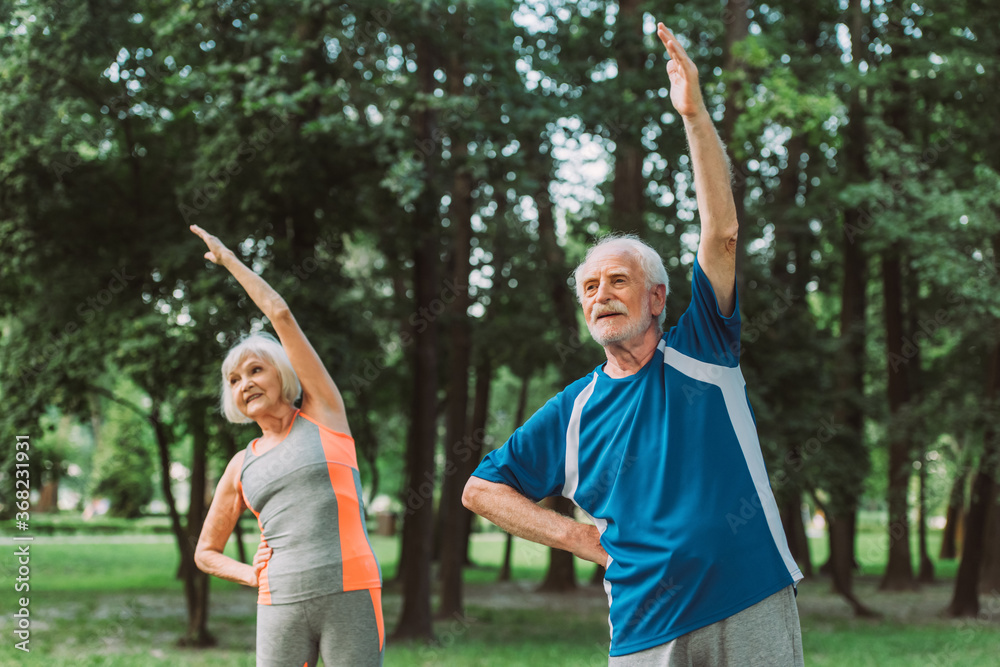 Selective focus of senior man exercising near smiling wife in park
