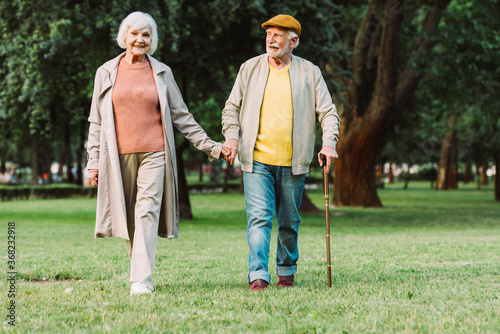 Positive senior couple holding hands while walking in park