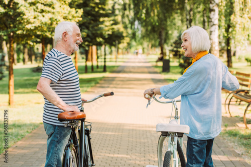 Senior woman looking at smiling husband while standing near bicycle in park © LIGHTFIELD STUDIOS