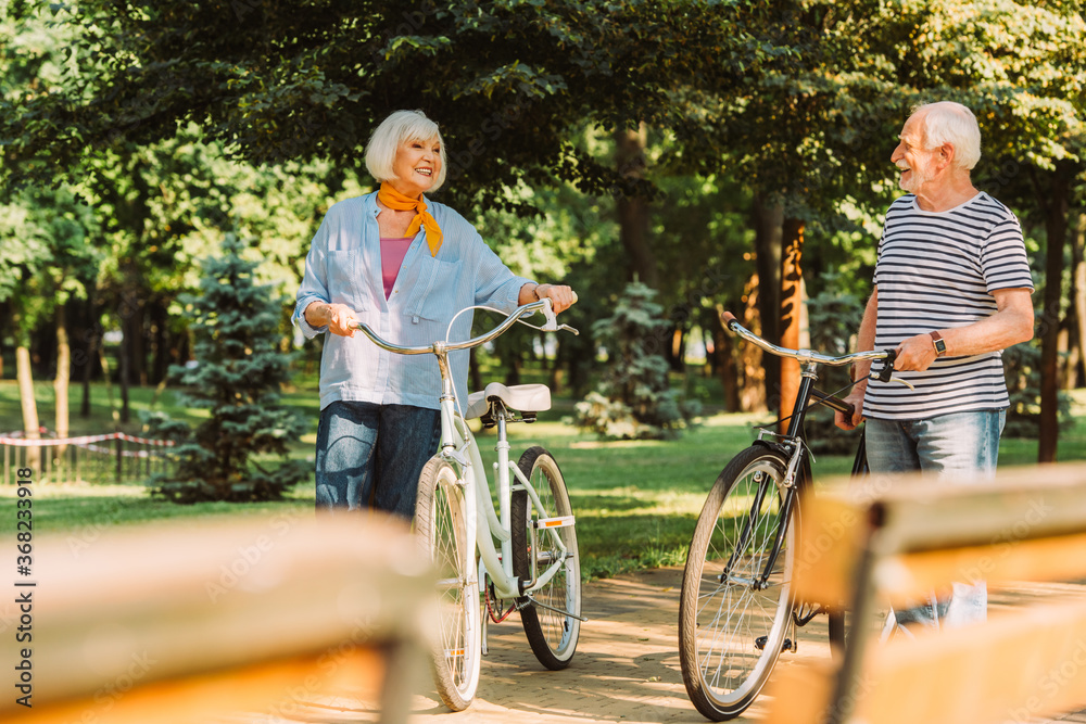 Obraz premium Selective focus of positive senior couple with bicycles walking in park