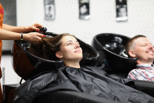 A married couple at the hairdresser washes their hair before a haircut. Hairdresser is washing the hair of a young woman