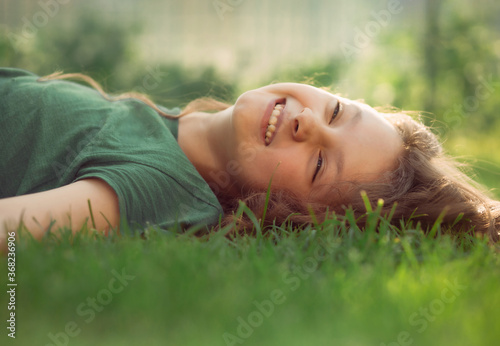 Happy smiling relaxing casual kid girl lying on the grass on nature summer background. Closeup positive outdoors