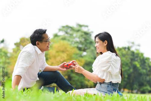 Man Giving Gift To Woman While Sitting On Grassy Field At Park