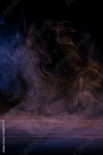 Conceptual image of multi-colored smoke isolated on dark black background and wooden table.