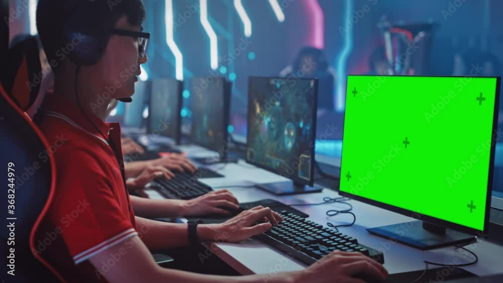Professional Gamer Plays in a Video Game with Mock-up Green Screen Display on a Championship. Team of Pro Gamers in Stylish Neon Cyber Games Arena. Online Broadcasting of Tournament. Side View