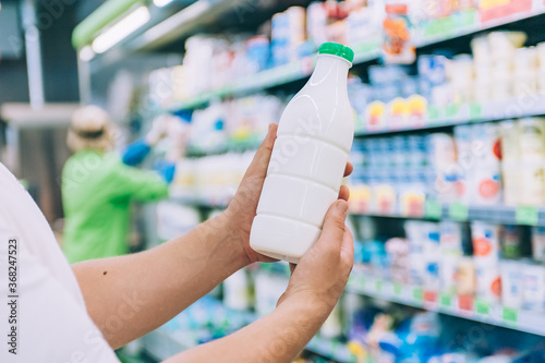 A man holds milk in a plastic bottle in his hands in a supermarket.
