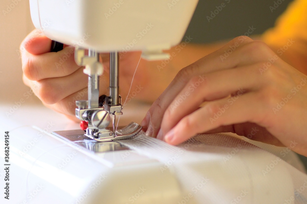 The process of sewing curtains from a mesh of white fabric. The rolled edge of the fabric is placed under the presser foot of the sewing machine. Close up view.