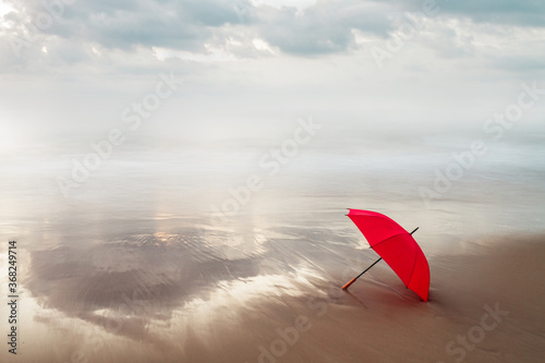 paraguas rojo en la orilla del mar con un cielo cargado en un amanecer
