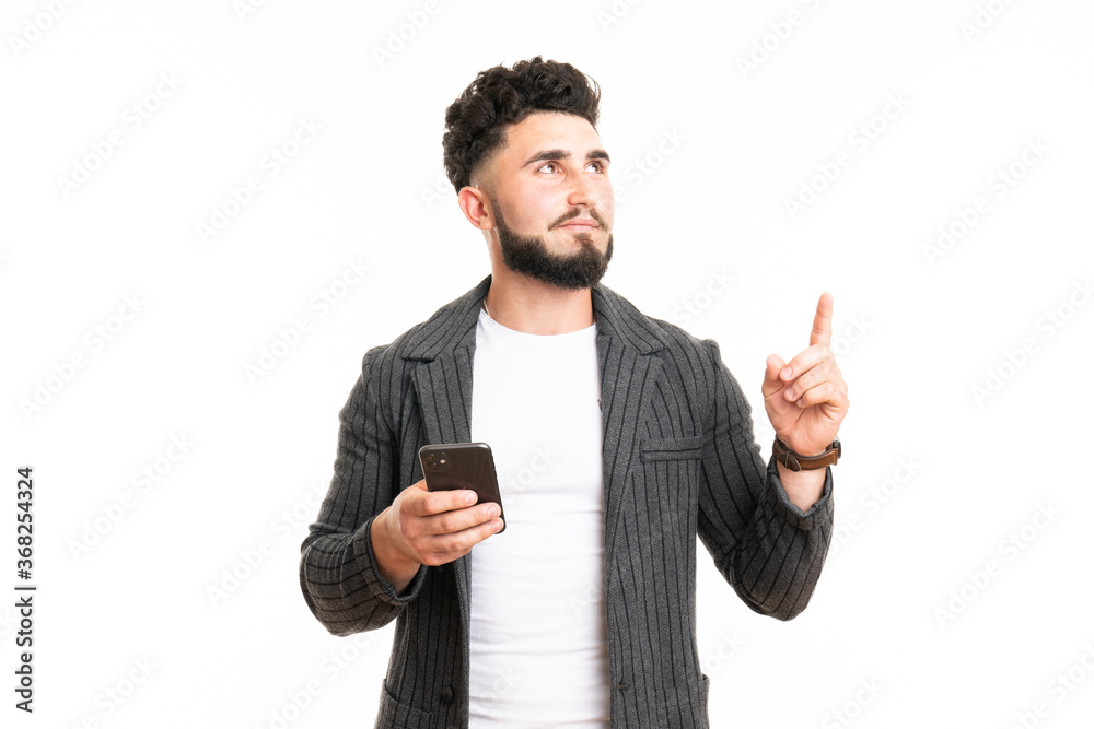 Portrait of an excited young man in casual using mobile phone while pointing finger up isolated over white background Portrait of an excited young man in casual using mobile phone while pointing finger up isolated over white background