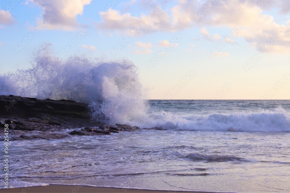 Powerful splash from wave crashing against rocks at sunset