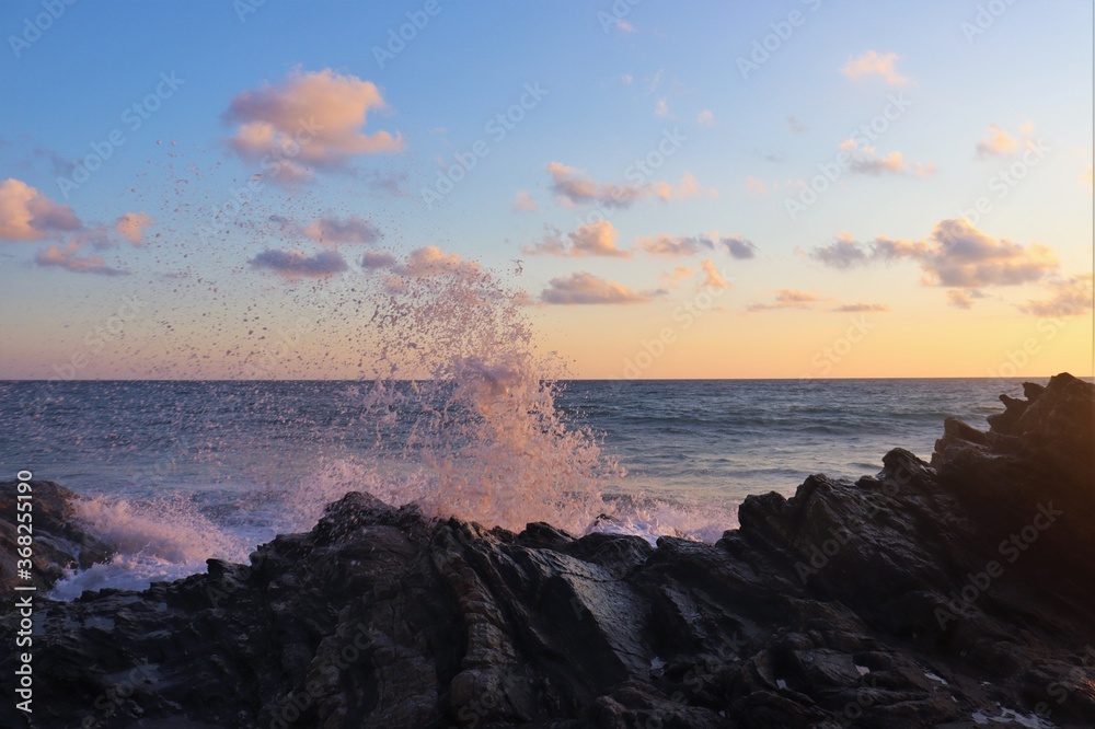 Big water splash on rocks into the sunset sky with ocean and horizon in the background