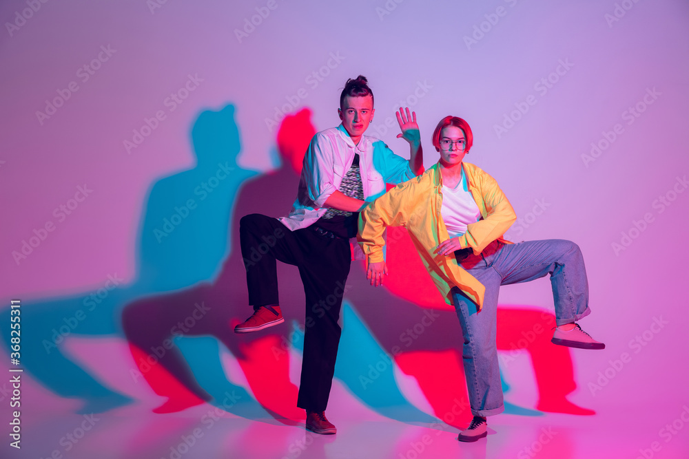 Obraz premium Young man and woman, couple dancing hip-hop, street style isolated on studio background in colorful neon light. Fashion and motion, youth, music, action concept. Trendy clothes. Copyspace for ad.