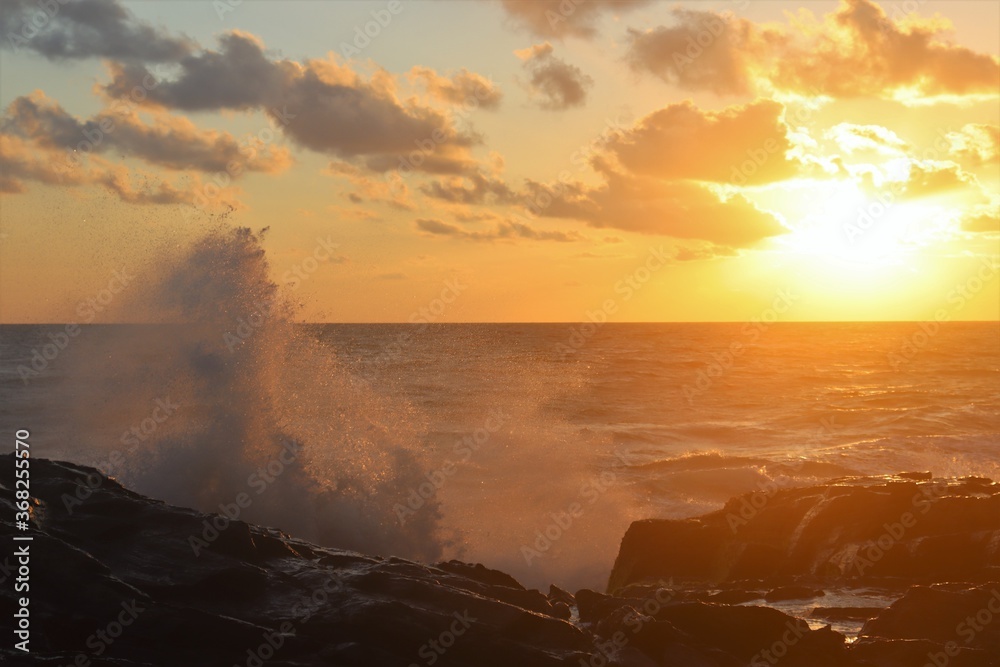 Giant splash from wave crashing against rocks at sunset