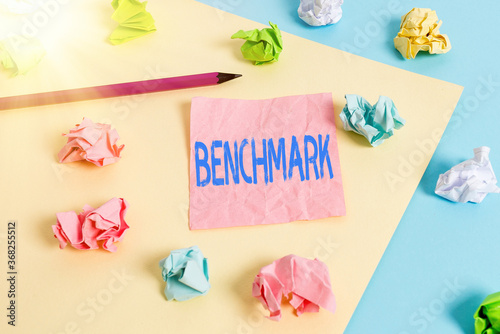 Conceptual hand writing showing Benchmark. Concept meaning something that serves as a standard by which others may be measured Colored crumpled papers empty reminder blue yellow clothespin © Artur