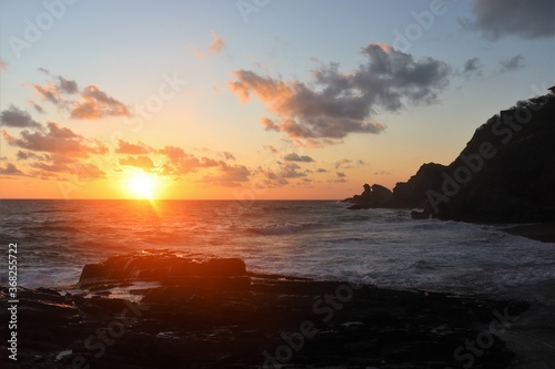 orange sun touching the sea surface at sunset at beautiful rocky coast