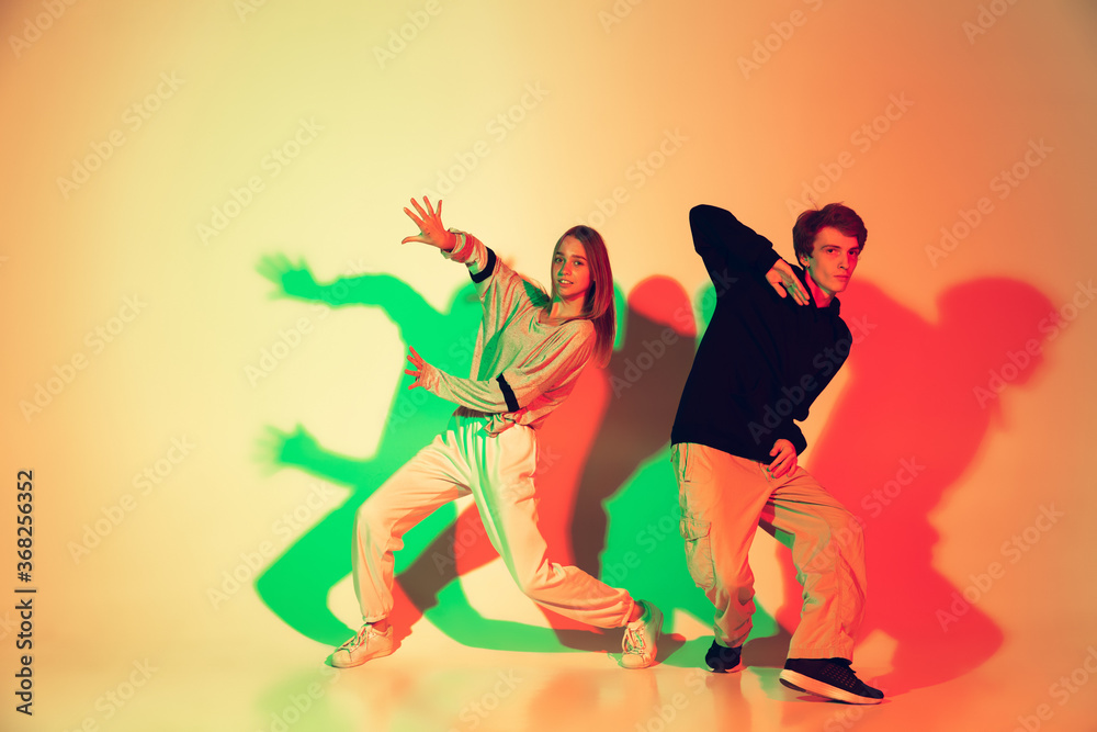 Young man and woman, couple dancing hip-hop, street style isolated on studio background in colorful neon light. Fashion and motion, youth, music, action concept. Trendy clothes. Copyspace for ad.