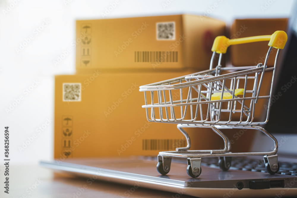 Shopping cart or trolley  on a notebook computer placed in front of the parcel box for delivery to customers. Commercial transactions conducted electronically on the Internet for distance selling.