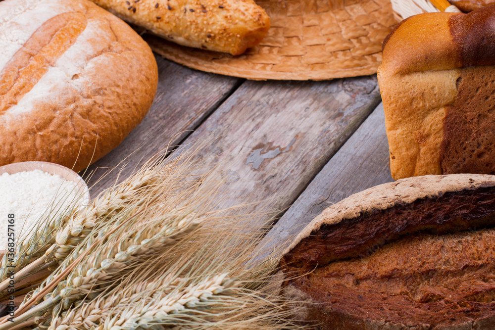 Assorted fresh bread and wheat ears. Homemade bread assortment and wheat spikelets on rustic wooden table. Space for text.