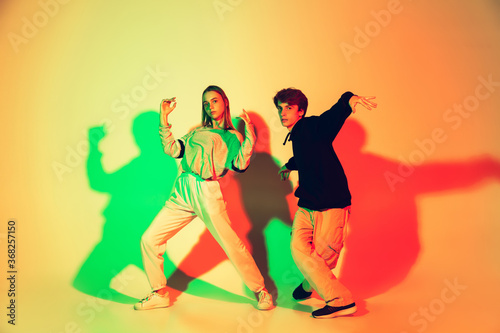 Young man and woman, couple dancing hip-hop, street style isolated on studio background in colorful neon light. Fashion and motion, youth, music, action concept. Trendy clothes. Copyspace for ad.
