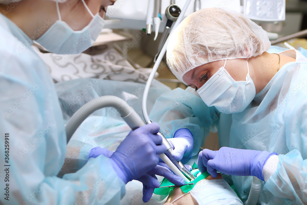 A dentist and an assistant perform an operation to treat deep caries in a child under General