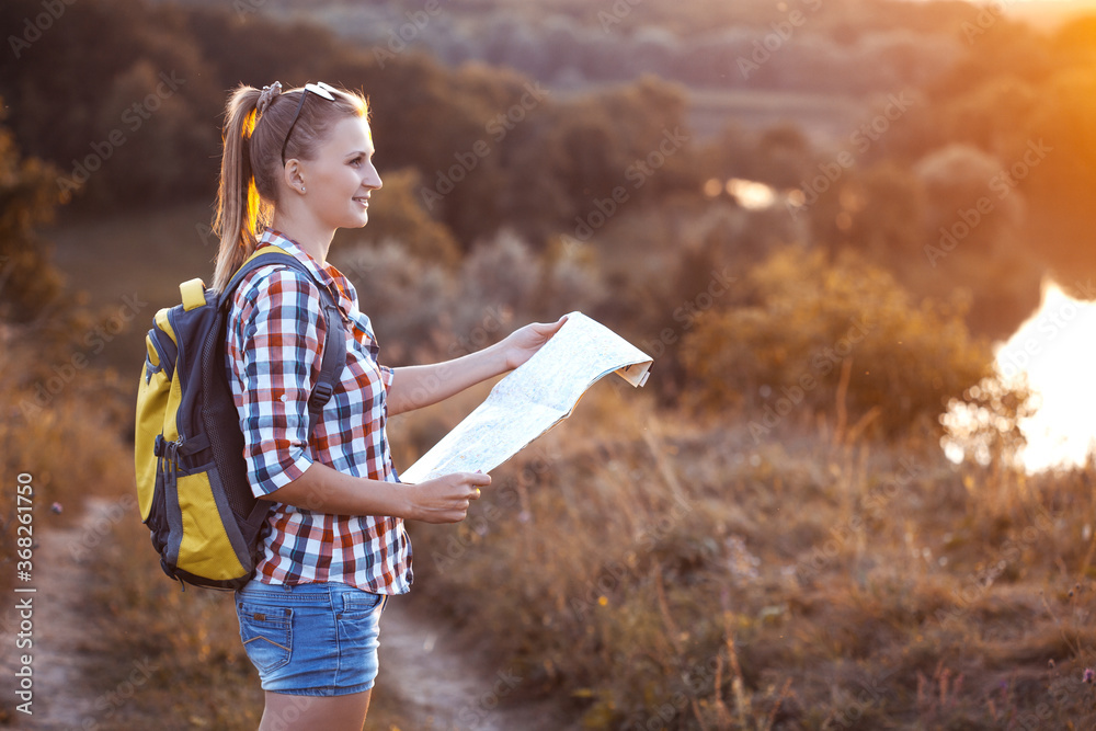 woman tourist with a map and a backpack on a hike navigates the terrain. Leisure