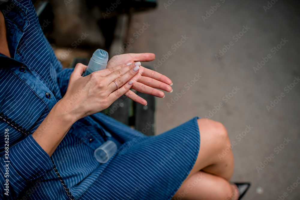 Young woman disinfects hands with a hand sanitizer outdoors 