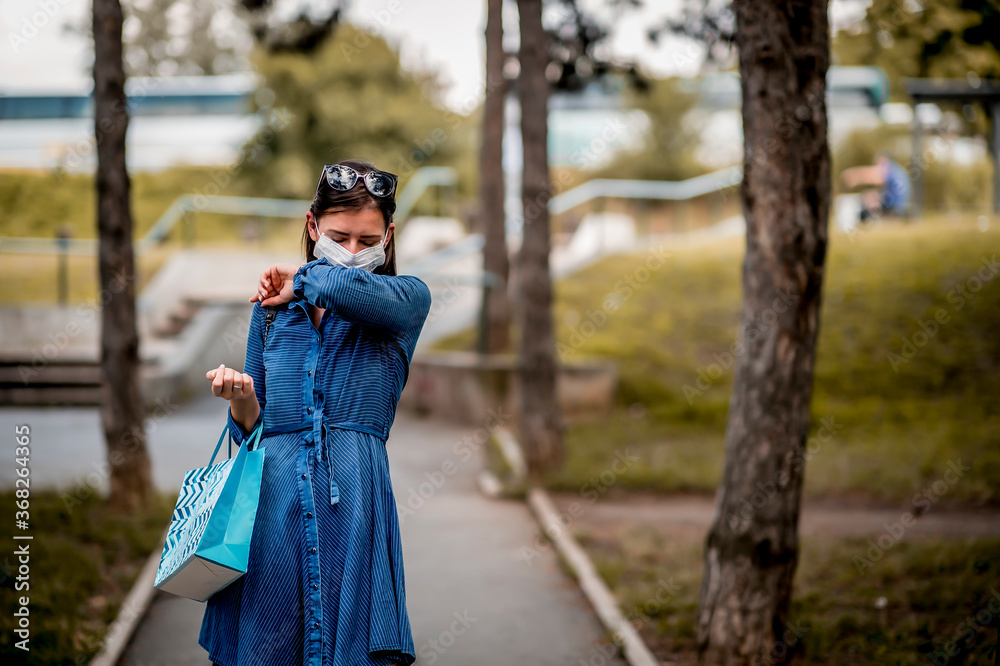 Woman with face mask sneezing into elbow while walking Woman with face mask sneezing into elbow while walking