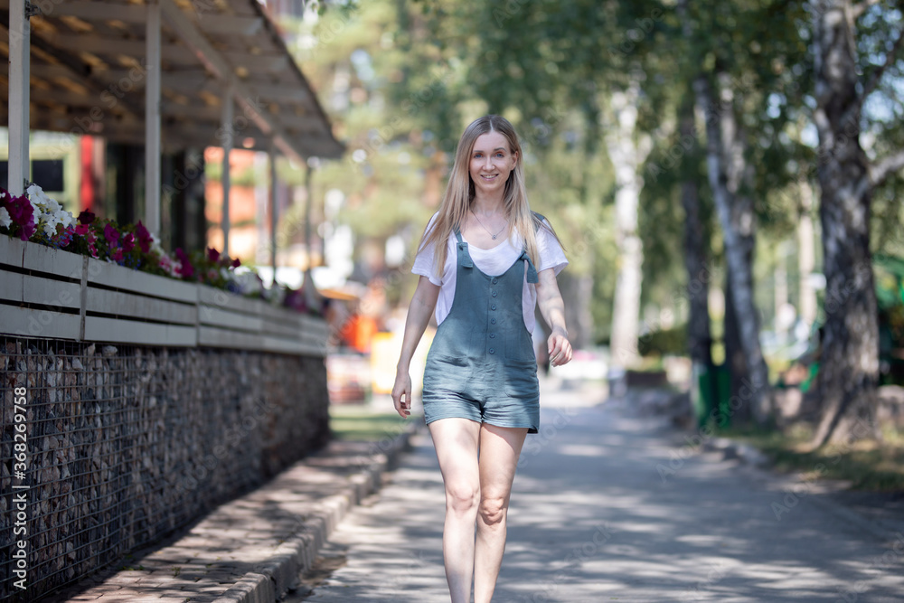 girl in overalls walks in the summer on the street