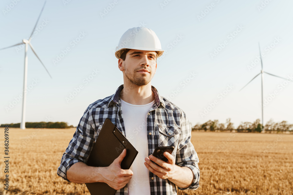 Fototapeta premium An electrical engineer standing on a field with windmills
