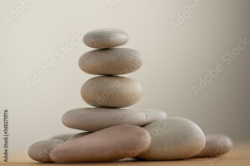 One simplicity stones cairn isolated on white background, group of light gray pebbles built in tower, wood table