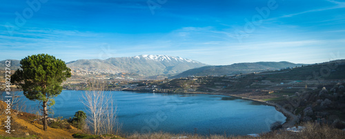 Beautiful panoramic view of Lake Ram  Birkat Ram  - a crater lake  maar  in the northeastern Golan Heights  with a Druze town of Majdal Shams and a snow-capped Mount Hermon in the background