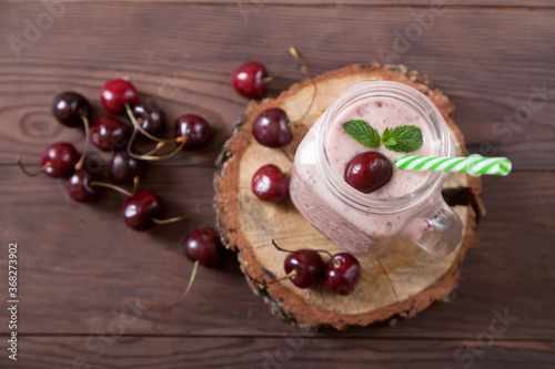 Sweet cherry smoothies in a jar with a straw, scattered berries on a wooden background. Vegetarian food. Healthy eating.