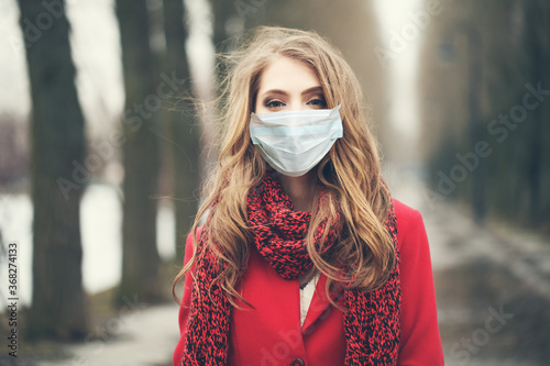 Beautiful young woman in medical protective face mask walking outdoors