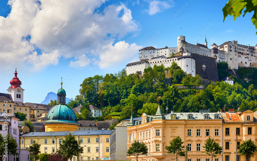 Fototapeta premium Fortress Salzburg (Festung Hohensalzburg).Austria, Salzburger Land. Medieval Castle at Cliff among summer trees under Old Town Buildings and church towers. Famous Landmark. Blue Summer Sky with Clouds