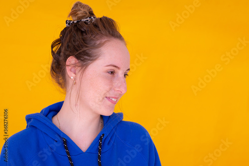 teen girl with messy bun and blue hoody against yellow background photo