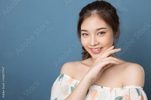 Beauty head shot of young asian woman on blue back ground. She is wearing colorful dress. She is touching her ear.