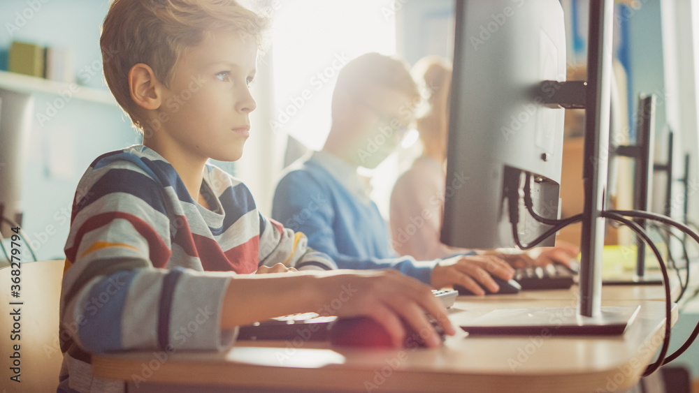 Elementary School Computer Science Classroom: Smart Little Boy Uses Personal Computer, Learning How to Use Internet Safely, Programming Language for Software Coding. Modern Education. Portrait View Elementary School Computer Science Classroom: Smart Little Boy Uses Personal Computer, Learning How to Use Internet Safely, Programming Language for Software Coding. Modern Education. Portrait View