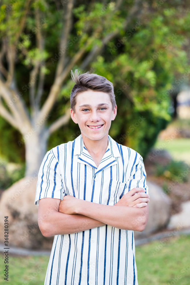Young teenage boy standing with arms crossed smiling in garden Young teenage boy standing with arms crossed smiling in garden