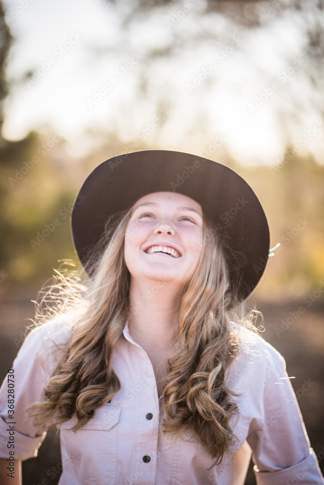 Teenage girl throwing head back laughing wearing akubra hat on farm in