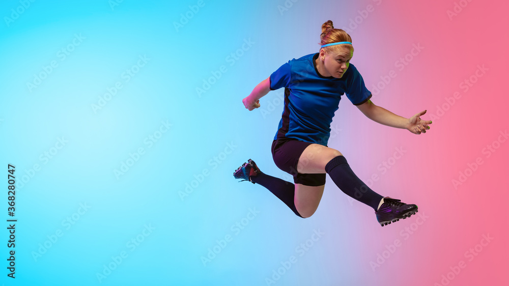 High jumping. Female soccer, football player training in action isolated on gradient studio background in neon light. Concept of motion, action, ahievements, healthy lifestyle. Youth culture.