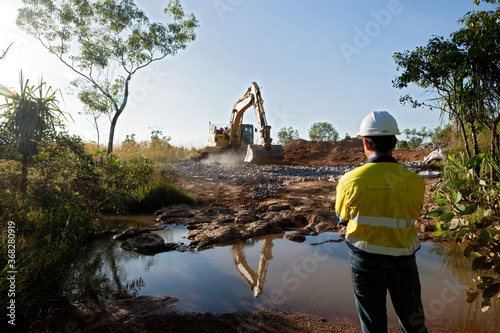 Industrial worker overseeing a large digger moving rocks on an industrial building site