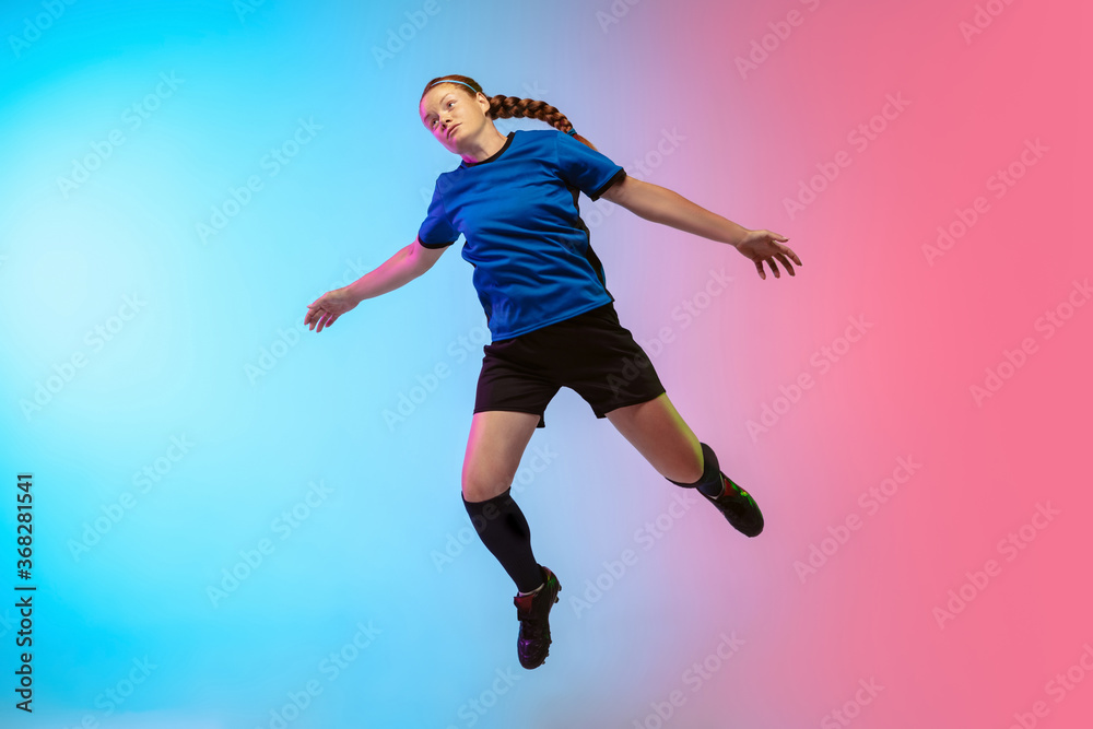 Obraz premium High jumping. Female soccer, football player training in action isolated on gradient studio background in neon light. Concept of motion, action, ahievements, healthy lifestyle. Youth culture.