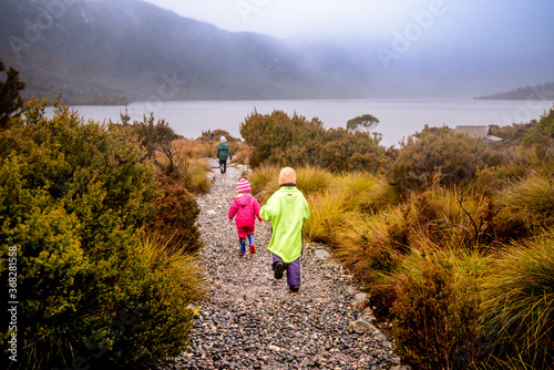 Children in bright rain jackets running down path on overcast day